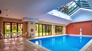 Ein Innenpool mit Dachfenster, Steinböden und Blick ins Freie.