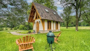 A small wooden house with a sloped roof, surrounded by lush green grass and trees. - Experience a Regenerative Farm in a New Tiny Home (Nixa)