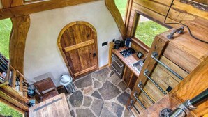 A rustic kitchen with wooden walls and a stone floor, featuring a sink, stove, and various kitchen utensils. - Experience a Regenerative Farm in a New Tiny Home (Nixa)