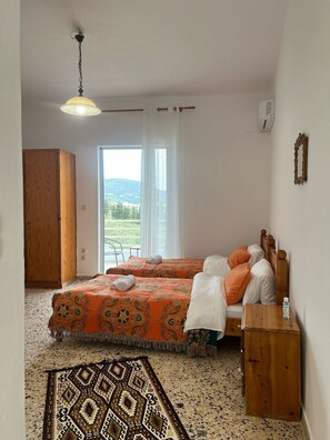 Une chambre avec deux lits, une armoire en bois, une petite table, un luminaire suspendu et une fenêtre donnant sur un paysage verdoyant.