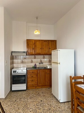 Une cuisine de taille réduite, dotée de meubles en bois, d’un réfrigérateur blanc, d’une cuisinière et d’un luminaire suspendu.