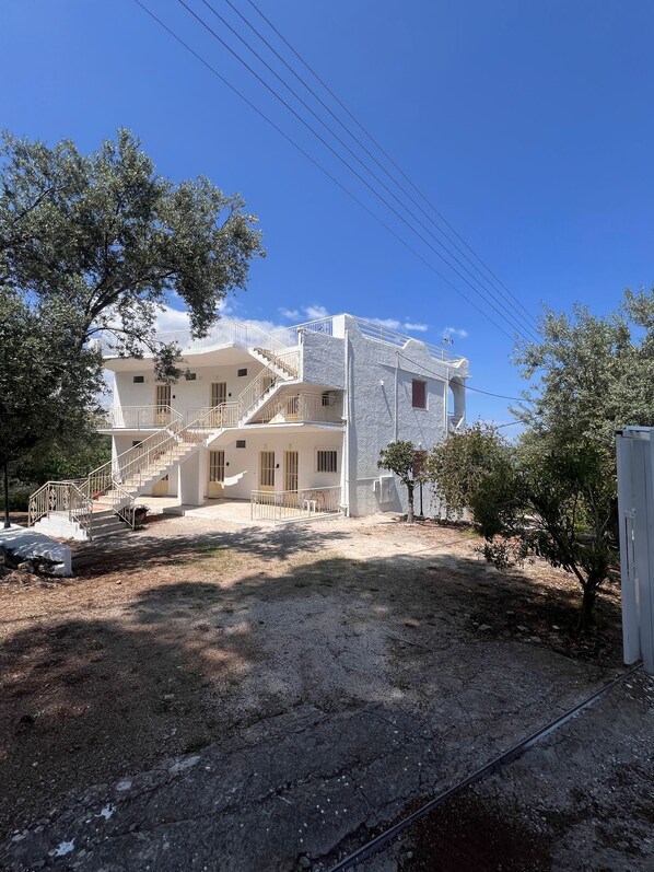 Un bâtiment à deux étages, avec un escalier menant à l’étage supérieur, entouré d’arbres et sous un ciel dégagé.