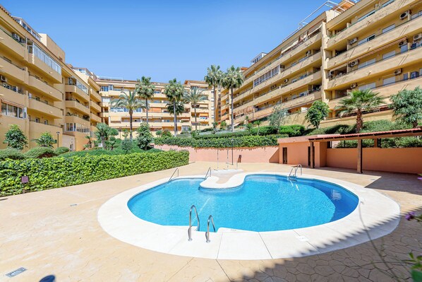 A swimming pool surrounded by a landscaped area with palm trees and a multi-story building in the background. - Brisa Marina luxury apart in fuengirola near the beach (Fuengirola)