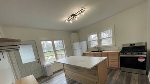 A kitchen with a central island, a stove, a refrigerator, and a window with a view of the outdoors. - Charming 1900 home with furnished kitchen and king bed (Lake Mills)