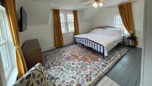 A bedroom with a bed, a ceiling fan, a window with curtains, a rug, and a small table with a lamp. - Charming 1900 home with furnished kitchen and king bed (Lake Mills)