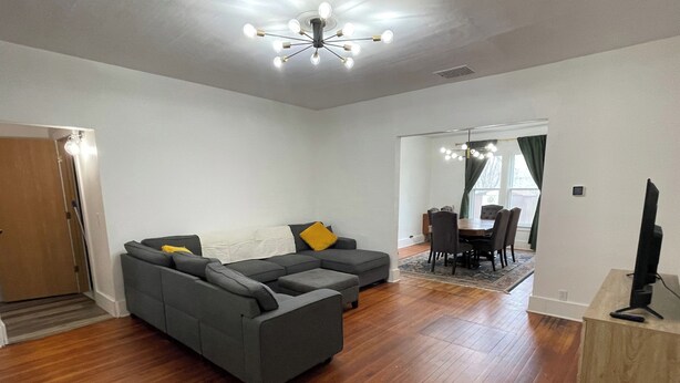 A modern living room with a gray sectional sofa, a dining area with a wooden table and chairs, and a TV on a stand. - Charming 1900 home with furnished kitchen and king bed (Lake Mills)
