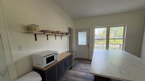 A kitchen with a white microwave, a trash bin, a wooden cabinet, and a marble countertop. - Charming 1900 home with furnished kitchen and king bed (Lake Mills)