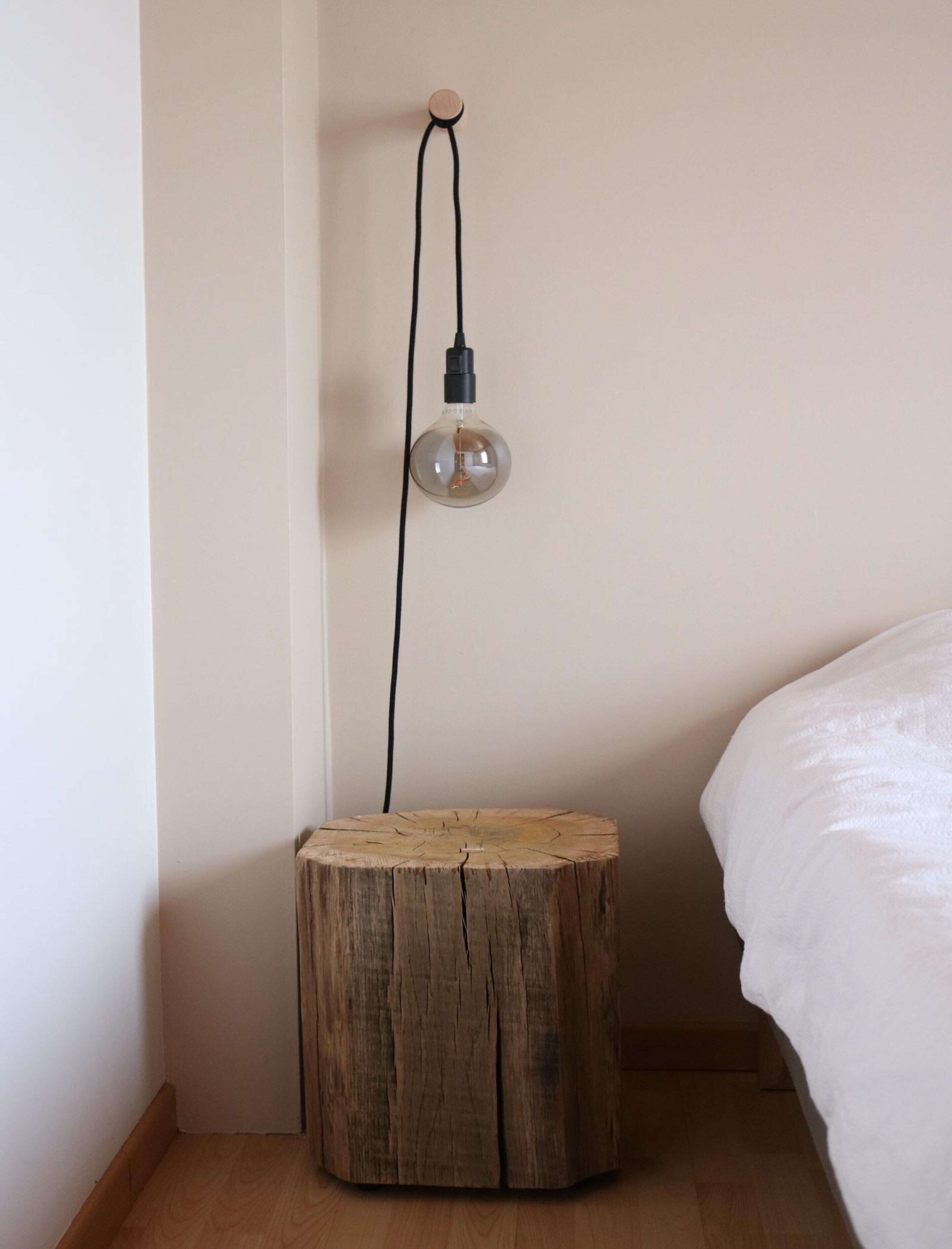 A round wooden stool with a light bulb hanging from a cord on the wall.