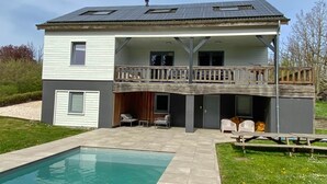 Ein zweistöckiges Haus mit Balkon, Schwimmbad und Sitzgelegenheiten im Freien.