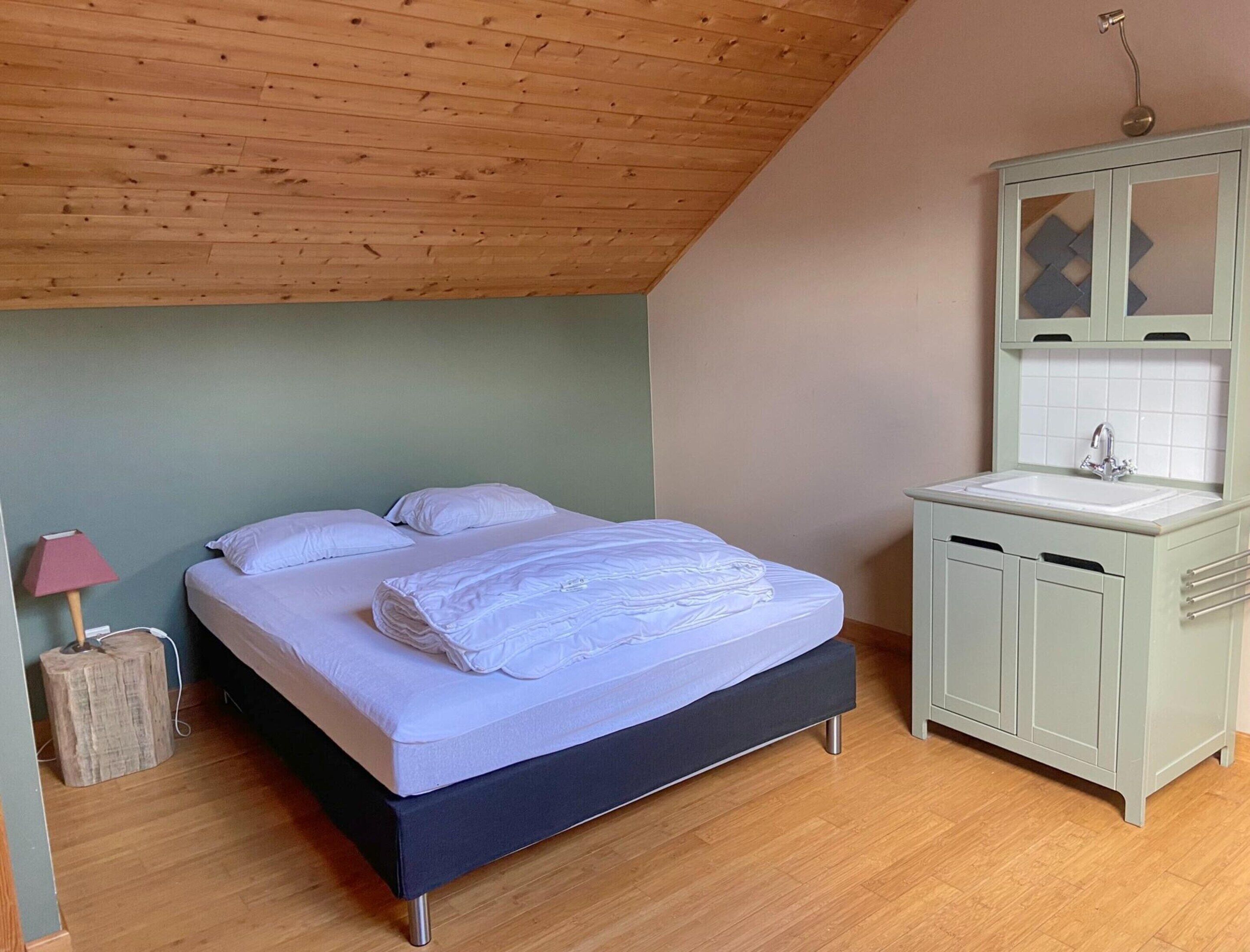 Ein Schlafzimmer mit einem Bett, einem Nachttisch, einer Lampe und einem kleinen Schrank mit Spiegel.