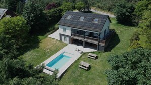 Ein zweistöckiges Haus mit Solardach, Schwimmbecken und einer Terrasse mit Sitzgelegenheit.