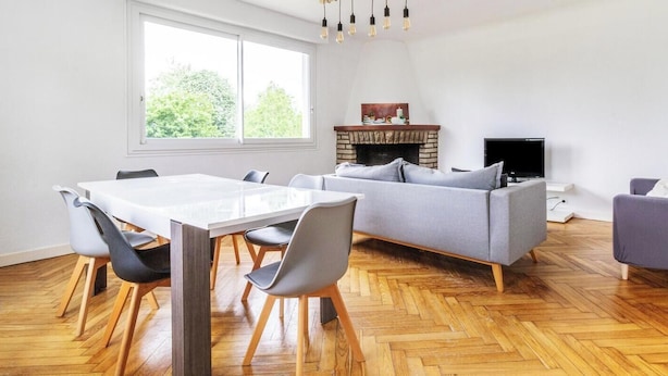 A spacious living area with a white table, grey sofas, and a fireplace.