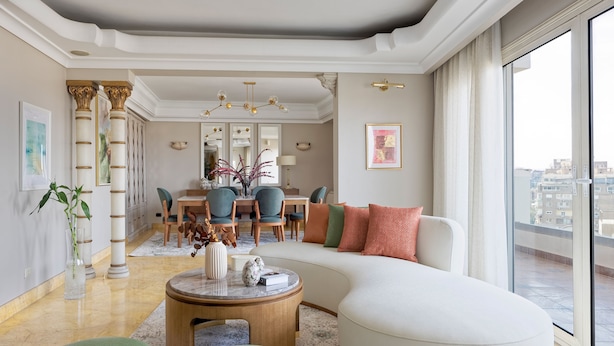 A spacious living room with a large white sofa, a round coffee table, and a dining area with blue chairs and a chandelier. - VESTA - Nile Zamalek Residence (Cairo)