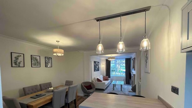 Eine moderne Küche mit einer zentralen Kochinsel, Pendelleuchten und einem Essbereich mit Holztisch und -stühlen.