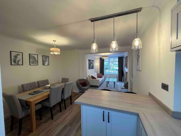 Een moderne keuken met een centraal eiland, hanglampen, en een eethoek met een houten tafel en stoelen.