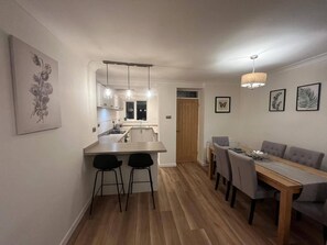 Een moderne keuken met hanglampen, een eethoek met een tafel en stoelen, en een gang naar een deur.