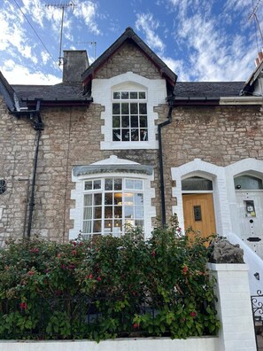 A stone building with a pitched roof, a central bay window, and a front door.