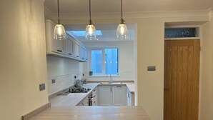 Eine moderne Küche mit einer zentralen Kochinsel, Pendelleuchten und Blick ins Freie durch ein Fenster.
