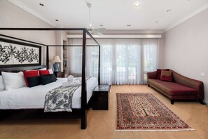 A four-poster bed with a canopy, a red sofa, a patterned rug, and a large abstract painting on the wall.