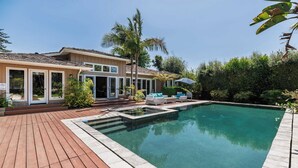 Una piscina con cubierta de madera, una casa con techo de tejas y palmeras.