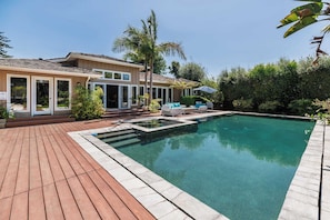 A swimming pool with a wooden deck, a house with a tiled roof, and palm trees. - La Jolla Retreat: Pool, Tennis, & Walk to Beach (San Diego)