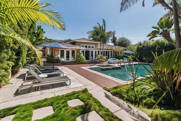 A house with a swimming pool, outdoor furniture, and lush greenery.