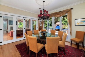 A dining area with a glass table surrounded by six chairs, a chandelier, and a red patterned rug.