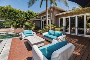 A spacious outdoor deck with a pool, white wicker furniture, and a large sliding glass door leading to a covered patio area. - La Jolla Retreat: Pool, Tennis, & Walk to Beach (San Diego)