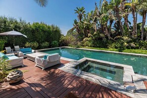 A pool area with lounge chairs, a hot tub, and lush tropical vegetation.