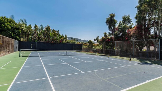 Una cancha de tenis con una red, rodeada por una valla y follaje.