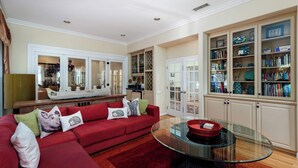 Un salón con un sofá rojo, una mesa de centro de cristal y una estantería llena de libros y objetos decorativos.