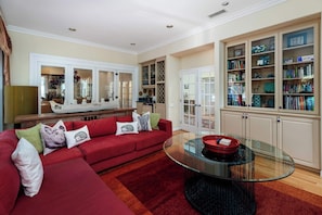 A living room with a red sofa, a glass coffee table, and a bookshelf filled with books and decorative items. - La Jolla Retreat: Pool, Tennis, & Walk to Beach (San Diego)