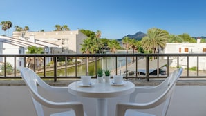 A balcony with a table set for two, overlooking a body of water and buildings. - Apartamentos Venecia  (Alcúdia)