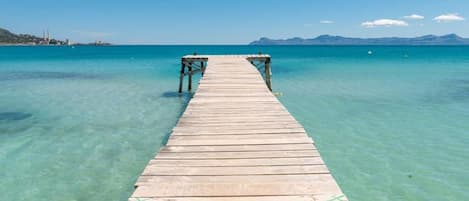 A wooden pier extending into clear turquoise water with a distant mountain range.