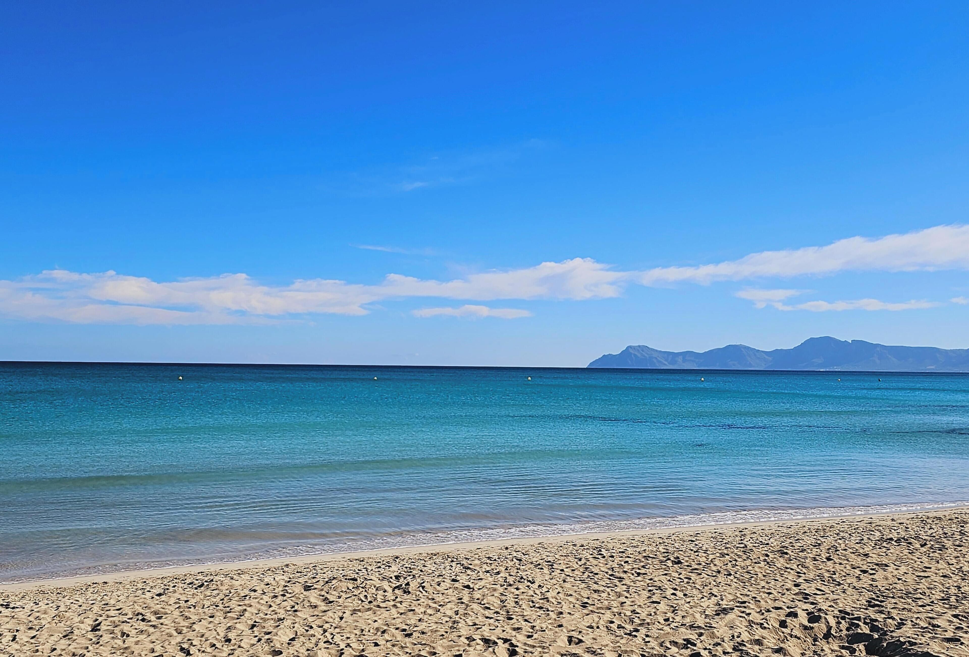 A beach with clear blue water and a distant mountain range.