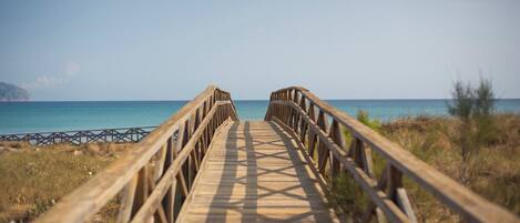 A wooden boardwalk leading to a beach with clear blue water and distant land.