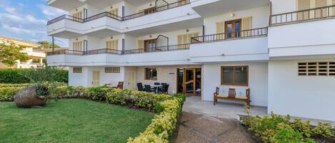 A multi-story residential building with balconies, a garden area, and outdoor seating.