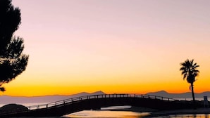 A calm waterfront at sunset with a bridge, a palm tree, and a bench. - Apartamentos Venecia  (Alcúdia)