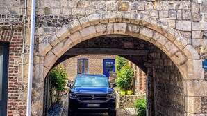Un arc en pierre mène à un espace de stationnement où une voiture bleue est garée en dessous.