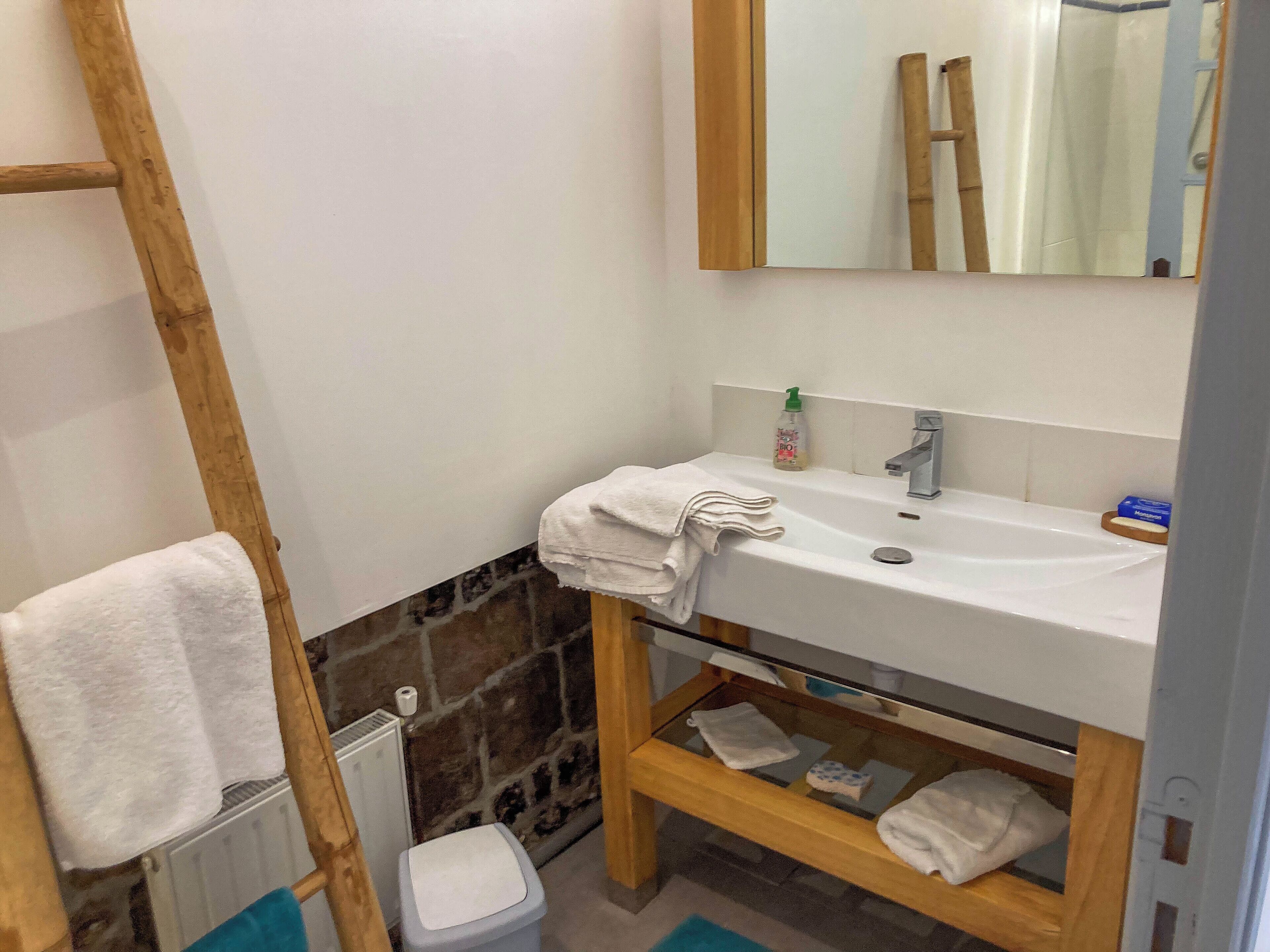 Une salle de bain avec un lavabo blanc, un miroir, un porte-serviettes et une étagère en bois.