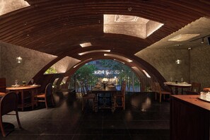 A restaurant with a high, arched ceiling and a view of a garden. Tables and chairs are arranged for dining. - Anima - Vietnamese Contemporary Art Boutique Hotel (Ho Chi Minh City)