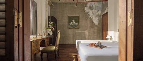 Une chambre d’hôtel avec un lit en bois, un bureau avec une chaise, un tableau au mur et un plancher en bois.