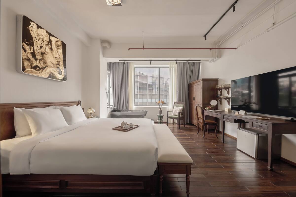 A hotel room with a large bed, a desk with a TV, a chair, and a window with curtains.