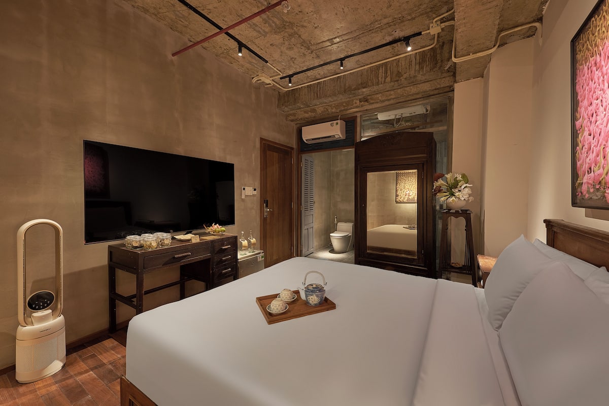 A hotel room with a large bed, a flat-screen TV, a desk with a mirror, and a bathroom visible through an open door.
