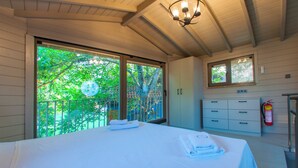 A hotel room with a bed, a nightstand, a window with a view of trees, a ceiling light, and a fire extinguisher. - Junior Garden Villa (Sapanca)