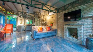 A spacious living area with a grey sofa, a television mounted on a brick wall, and a fireplace. - Junior Garden Villa (Sapanca)