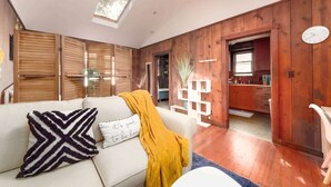 A cozy living room with a sofa, a yellow throw blanket, and a decorative pillow. A wooden cabinet and a kitchen area are visible in the background. - Downtown Studio Garden Cottage | Near UC + Parking (Berkeley)