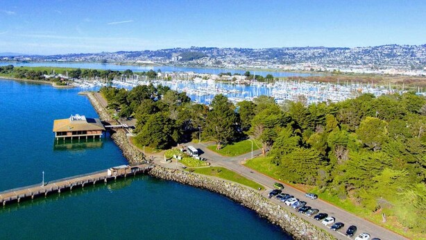 An aerial view of a marina with boats, a dock, and a parking area with cars. - Downtown Studio Garden Cottage | Near UC + Parking (Berkeley)