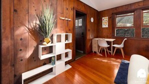 A room with wooden walls, a white shelving unit, a dining area with a table and chairs, and a window with a view. - Downtown Studio Garden Cottage | Near UC + Parking (Berkeley)