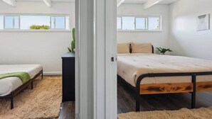 A bedroom with a bed, a bench, a plant, and a window.